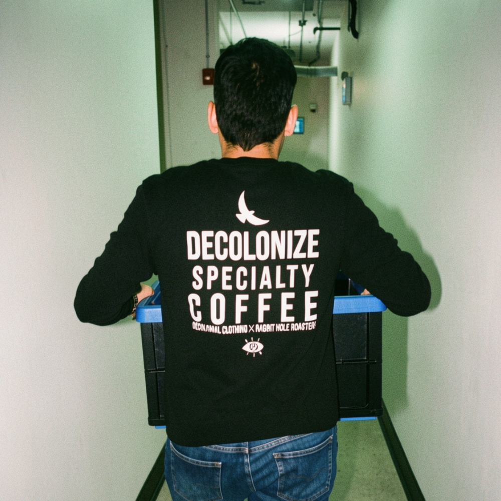 David Lalonde from Rabbit Hole Roasters sporting his black long sleeve tshirt printed by Decolonial Clothing with 'Decolonize Specialty Coffee' on his back, walking in a hallway.